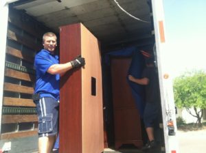 Man in a blue shirt moving a brown shelf unit from a moving truck.