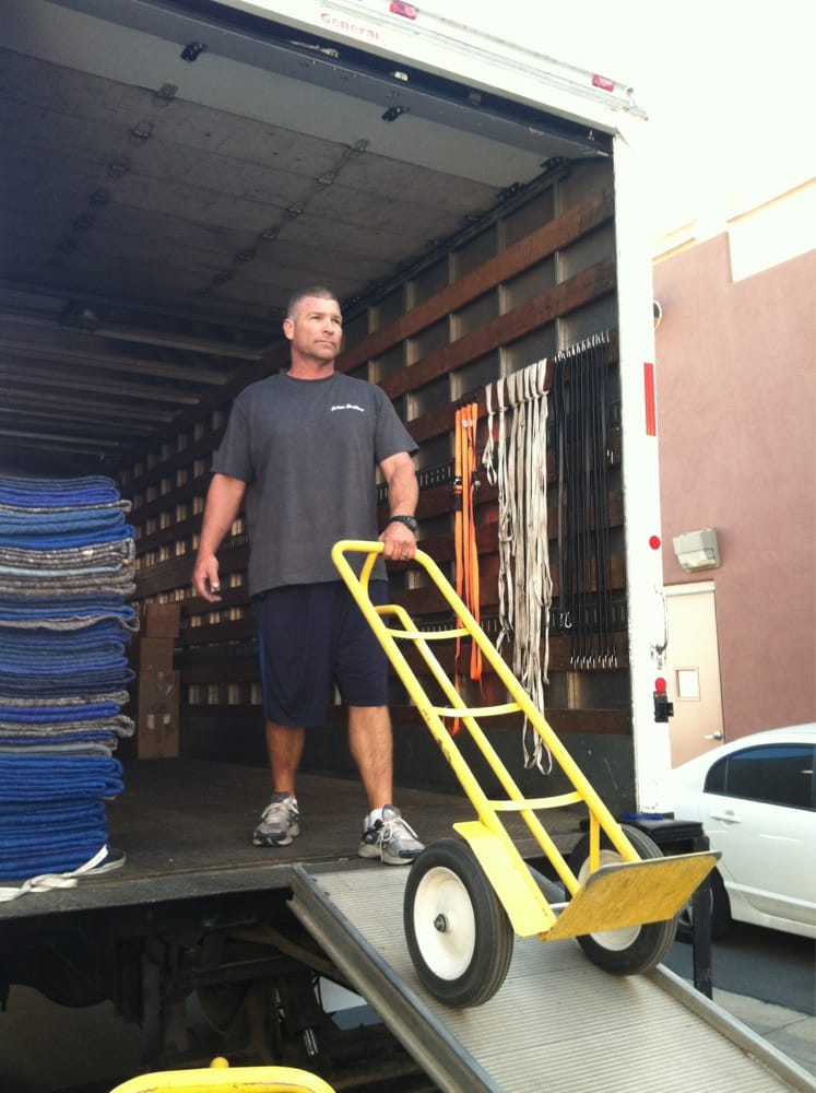 A man with a yellow moving dolly on the ramp of a moving van.