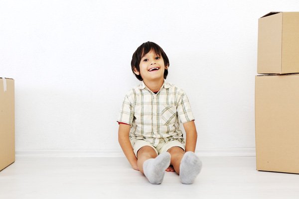 A smiling boy sitting on the ground between moving boxes.